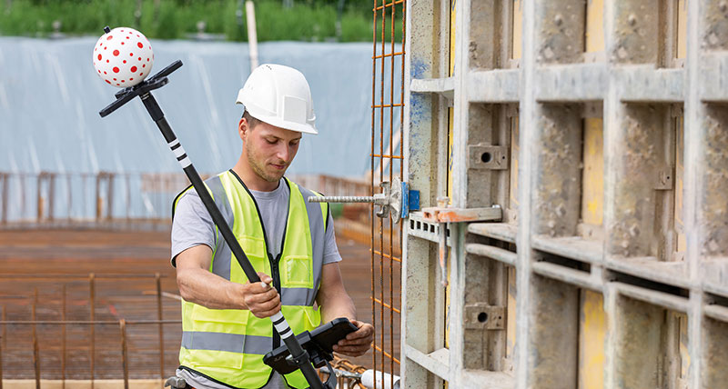 Construction worker with white hart had and Leica iCON tilted Leica iCON vPole on construction site.